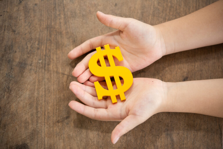 Child's hands gently holding a bright yellow dollar sign symbol representing the financial security and stability that guaranteed lifetime income annuities provide for special needs planning.